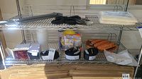 Metal shelving unit with various items: tie down straps, forearm forklift straps, baseball gloves, and packing materials.