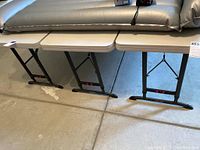 Three beige folding utility tables with black metal legs arranged side by side in garage setting.