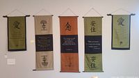 Five fabric wall hangings displayed side by side on a wall showing different colors and quotes