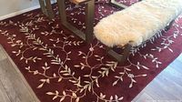 Full view of the rectangular deep red wool rug under a dining table with a cream-colored bench and gray legs.