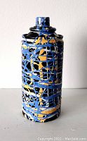 Photo showing front angle of the spray can sculpture with blue, yellow, and black abstract paint drips on metal surface