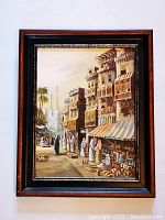 Frontal view of the framed painting showing a street scene with traditional buildings, people in Middle Eastern dress, and market stalls.