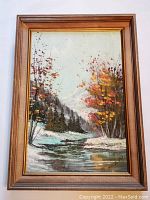 Framed painting showing full artwork and frame, with a river flanked by autumn-colored trees and mountain background.