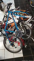 Assorted used bicycle and electric bike metal frames piled together on tiled floor. Blue frame prominently visible with crankset and rear wheel attached.