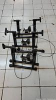Three black bike trainers positioned on tiled floor, view showing frames, clamps, and attached cables.