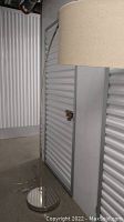 Full view of tall stainless steel floor lamp with canvas drum shade in storage unit.