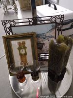 Photo of Bona signed painting in iron frame, candle, and two glasses grouped on reflective surface.