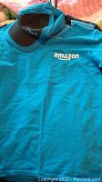 Blue Amazon T-shirt and black and blue cap with Amazon swoosh logo laid flat on bed