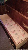 Open drawer showing floral lined interior and brass hardware on front.