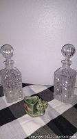 Two clear crystal bottles with stoppers and a small green ceramic elephant planter arranged on a checkered cloth.