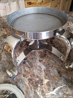 Photo of silver plated metal stand with four curved legs and round tray platform on a marble surface.