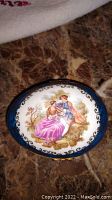 Top view of Limoges porcelain trinket box lid showing the detailed painting of the serenading couple with a blue border and gold accents.