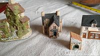 Four miniature village building pieces arranged on a gray surface showing details and scale.