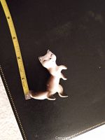 Porcelain Siamese cat figurine on a black surface with tape measure showing about 2 inches tall.