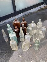 All 17 glass bottles arranged on the ground outside a building, showing variety of colors and sizes