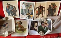 Multiple loose art prints laid out, predominantly Norman Rockwell style canvas prints showing various scenes involving people, with some prints rolled and some showing everyday life scenes.