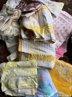 Photo showing a pile of assorted vintage bath towels in white, yellow and pink tones with different patterns including floral and geometric.