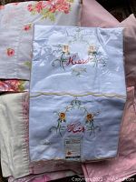 Various vintage bedding including embroidered His and Hers pillowcases and floral patterned fabrics.