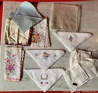 Overview of eight vintage handkerchiefs including embroidered floral designs and lace trims, arranged flat on white surface.
