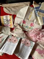 Lot of vintage linens including embroidered towels, mixer cover, embroidered and printed cloths, pink sheer fabric, and napkins.