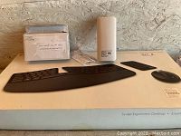Photo showing Microsoft Sculpt Ergonomic Desktop keyboard and mouse on box with charger and cable on box surface.