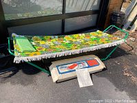Photo showing vintage hammock fully assembled with bright floral fabric, green metal frame, and original folded box underneath.