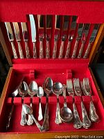 Overview of the cutlery set displayed in the open wooden case lined with red felt, showing knives, forks, spoons, and serving pieces.