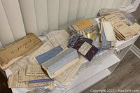 Wide shot of the collection of old letters and documents spread on a white surface, showing various sizes and types of papers bundled and arranged with visible aged edges and handwritten text.