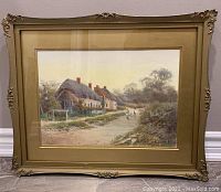 Framed watercolour painting showing a rural landscape with thatched cottages, a dirt road, and a figure with chickens.
