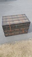 Full exterior view of antique wooden trunk with leather straps, metal locks, and visible wear.