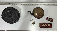 Full lot showing cast iron pot, antique crank doorbell with screws, and two OXO cubes tins on white surface with measuring tape.