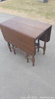 Front angled view of the antique wooden drop leaf table with leaves down on pavement outside.