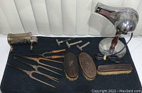 Full view of the antique styling tools including hair dryer, curlers, razors, and brushes laid out on black fabric.