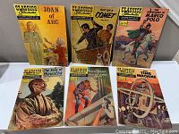 Six Classics Illustrated comic books arranged in two rows, featuring covers for Joan of Arc, Off on a Comet, The Adventures of Marco Polo, The Song of Hiawatha, The Hunchback of Notre Dame, and The Time Machine.