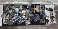 Wide overhead photo showing a collection of costume jewelry pieces in individual plastic bags spread on a dark surface including earrings, necklaces, and pins.