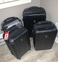 Four Heys hard shell suitcases arranged in a group, showing sizes, colors (black and silver), and overall condition.