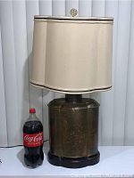 Full view of the large brass table lamp with fabric shade and wooden base alongside a 2-liter Coca-Cola bottle for scale.