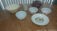 Full view of all items on wooden table showing various bowls, crocks, and pie plate