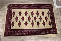 Full view of the Persian-style rug showing the central cream field with red diamond motifs and geometric patterned borders on a wood floor.