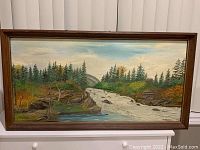 Full view of the framed oil painting depicting a waterfall in a natural landscape with trees and rocks.