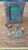 Full view of all sterling silver items including frame, brooches, chains, and pendants displayed on wooden surface.