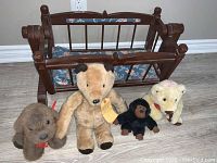 Wooden toy rocking cradle with four teddy bears lined up in front on the floor.