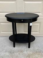 Full front view of black oval accent table showing top surface, drawer, legs and lower shelf