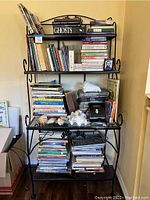 Front view of black wrought iron bakers rack filled with assorted books, seashells, and binoculars
