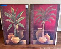 Two large canvas tropical art pieces depicting banana and palm trees with pottery, shown side by side against a wall.
