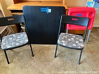 Full view showing black vinyl card table, two matching black metal folding chairs with fabric seats, and two red plastic TV trays stacked behind.