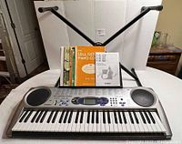 Front wide view of Casio LK-44 keyboard on adjustable stand with music books set in the music holder.