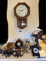 Photo showing Seiko wall clock, two additional clocks, vintage metal fan, rotary phone, carved turtle and elephants, and large wooden bowl.