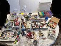 Wide view of crafting supplies including trays of beads, glue bottles, jewelry tools, beads in bags, and assorted crafting materials on a table.
