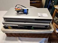 Two silver DVD players stacked in a basket with cables on top.